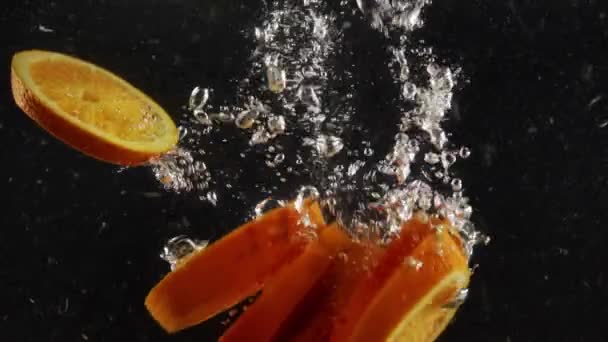 Шматочки Свіжих Апельсинів Занурюються Глибоко Воду Бризками Чорному Тлі — стокове відео