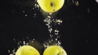 Temiz ve sağlıklı sarı elmaların yakın plan siyah zemin üzerinde büyük bir sıçrama ile berrak suya düşmesi