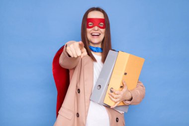Heyecanlı kadın süper kahraman kostümü ve maske takıyor mavi arka planda izole edilmiş klasörler seni ofis işi için süper takımına seçtiğini gösteriyor.
