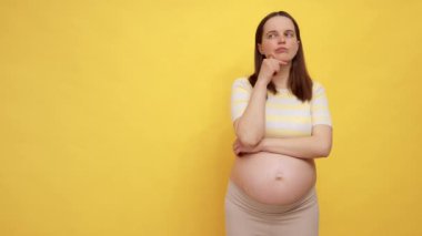 Sarı arka planda, çıplak göbekli, dalgın, beyaz, hamile bir kadın terfi için doğum fotokopisi çekmeyi düşünüyor.