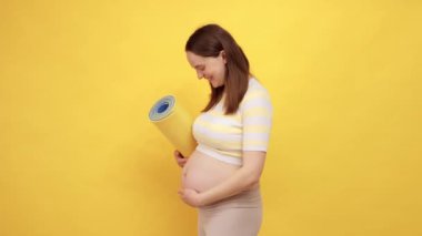 Karemat 'ın sarı arka planda izole edilmiş ve geçen üç aylık dönemde iç huzurunu kucaklayan çıplak göbekli, beyaz, hamile bir kadının yan görüntüsü.