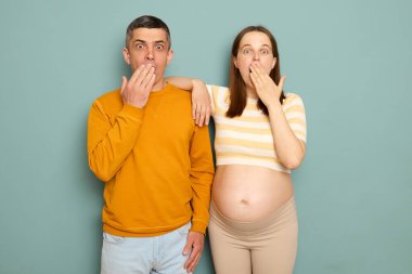 Şok olmuş aile, mavi arka planda yalnız bir bebek bekliyor. Kadın ve koca kameraya bakıyor. Ağızlarını avuç içiyle kaplayan büyük gözlerle.