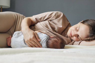 Emziren anne. Annem evi emziriyor. Anne sütü faydaları. Beyaz tenli güzel anne bebeğini yatakta emziriyor.