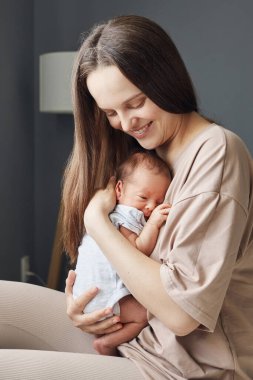 Gülümseyen, neşeli, beyaz bir anne yeni doğmuş bebeğini kucağında taşıyor mutlu bir anne kucağında bebeğini elleriyle tutuyor küçük oğluna sarılıyor.
