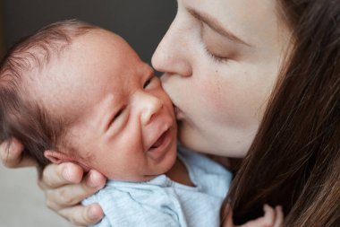 Nazik Kafkasyalı kahverengi saçlı genç anne, sağlıklı yeni doğmuş kadınını emziriyor. Ağlayan küçük çocuğunu öpüyor. Sevgi dolu bebeği annesinin kollarında huzur içinde dinleniyor.