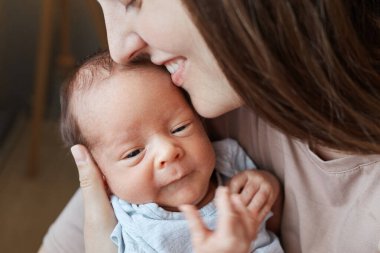 Şirin kahverengi saçlı genç bir kadın. Ağlayan küçük bir bebeğe yaslanıyor. Mutlu bir gülümsemeyle oturuyor.