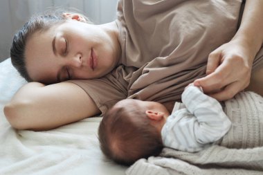 Evde emziriyorum. Evde emzirme. Uykulu yorgun anne bebeğini emzirirken, gözleri kapalı yatarken dinleniyor.