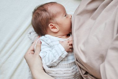 Tanımlanamayan genç bir kadın, bebeğini evde yatağında emziriyor. Bebek, çocuk odasında sağlıklı besleniyor.