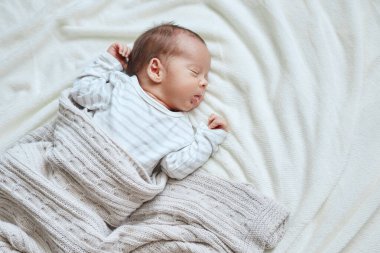 Küçük çocuklar için rahat bir yatak. Yeni doğan erkek bebek, gri örgü battaniyenin altında uyuyor. Yeni doğanlar için yatakta kestiriyor.