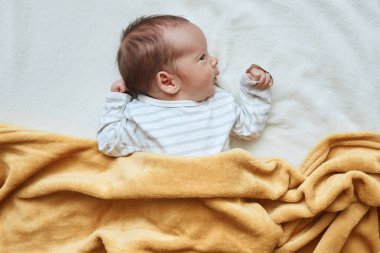 Bebek yatakta yatıyor. Çizgili çocuk kıyafetleri giyiyor. Sağlıklı yeni doğmuş, yumuşak sarı ekoseli kumaşın altında yatıyor.