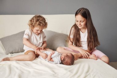 Sevimli kardeşlerin ilk buluşması evde yeni doğan erkek kardeşleriyle yatakta oturan çocuklar küçük kardeşlerine sevgi ve şefkatle bakıyorlar.