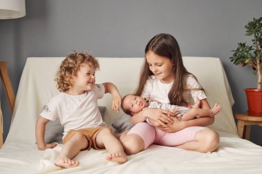 Neşeli kız kardeşler, günlük kıyafetlerini giyip yeni doğan erkek kardeşlerine ninni söylüyorlar.