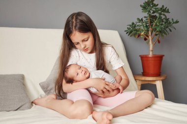 Kafkasyalı, sevimli, şirin abla sabah uyandığında yeni doğmuş bebeğiyle oynuyordu. Ablası, yeni yürümeye başlayan bebekle yatakta yatarken dalga geçiyordu.