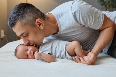Mutlu bir baba, yeni doğmuş bebeğini evde öpüyor. Yeni doğmuş bebeğini nazikçe kucaklıyor. Babalığının ilk anlarını sevgiyle anarak yatak odasında huzurlu bir bağ kuruyor.