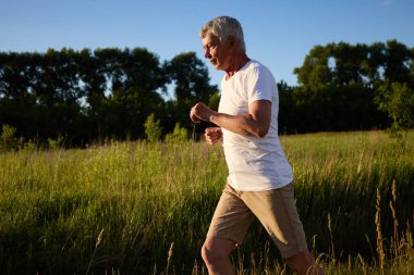 Kırsal kesimde koşan gümüş saçlı son sınıf öğrencisi. Açık hava egzersizi yapıyor. Parlak yaz sabahında sağlığını korumak için koşuyor.