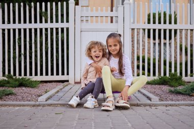 Neşeli, beyaz, sevimli, sevimli küçük kız kardeşler dışarıda oynuyorlar evinin önündeki tahtada oturup eğleniyorlar.