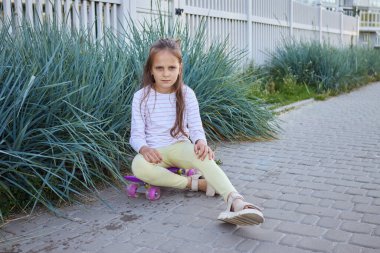 Kafası karışmış, kızgın küçük kaykaycı kız kameraya bakıyor ve bozuk para tahtasıyla zaman geçiriyor.