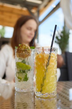 Bulanık, beyaz elbiseli, taze kokteylli bir kadın sıcak yaz gününde kafede oturuyor ve hafta sonları restoranda keyif çatıyor.