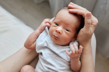 Meçhul kadın kucağında küçük oğlu ya da kızı açık gri elbiseli bebeğinin minik kafasını okşuyor. Evin içinde poz veriyor.