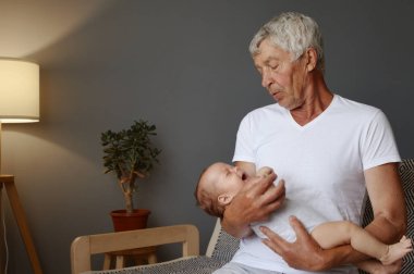 Büyükbaba ve torun kaynaşıyor. Yeni doğmuş torunu olan emekli bir adam. Yeni neslin mutluluğu. Beyaz saçlı büyükbaba yeni doğmuş bebeği evde uyutuyor.