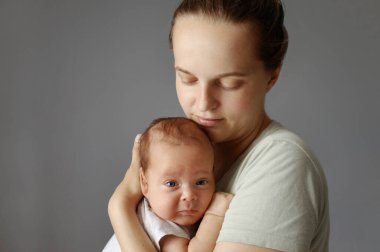 Ebeveyn bebekle oynuyor. Anne ve yeni doğan bebek. Kahverengi saçlı bir kadın, bir aylık bebeği kucaklıyor. Küçük bir çocuk ellerinde. Gri arka planda izole edilmiş.