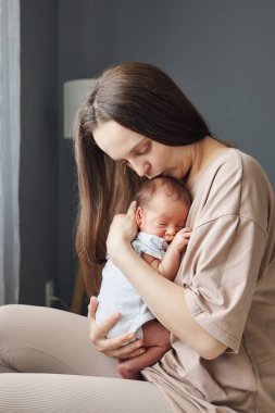 Kahverengi saçlı beyaz kadın, yeni doğmuş bebeğinin başını nazikçe öpüyor. Yeni doğmuş çocuğunun mutluluğunu ve güzelliğini yaşıyor. Sevgi dolu bir bağ ve ilgiyi yansıtıyor.