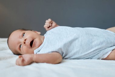 Yeni doğan, sevimli, esneyen bebek, beyaz ekose kumaş üzerinde yatar. Tulum giydirilmiş, boş bir yerde. Reklam için ya da terfi için kullanılıyor.