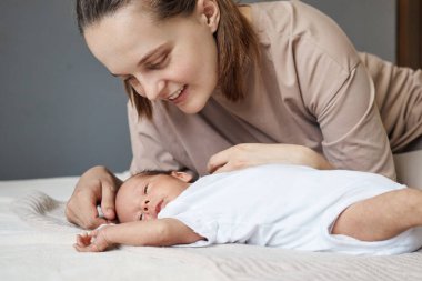 Sevgi dolu bir anne, yeni doğmuş bebeğiyle evde mutlu bir şekilde vakit geçirir. Annesi, küçük bebeğiyle birlikte bej tişört giyen kahverengi saçlı bir kadının yatağında uyuyakalır.