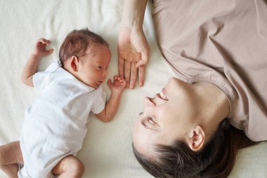 Yeni doğmuş bebeğiyle beyaz çarşafın üzerinde uzanmış gülümseyen siyah saçlı beyaz bir kadın değerli annelik anının tadını çıkarıyor ve evde kaynaşıyor.