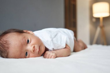 Yeni doğan bebek, reklam ya da tanıtım metni için vücudunda fotokopi alanı olan beyaz çarşaflı bebek yatağında karnının üstünde yatıyor.