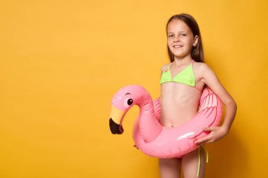 Flamingo şişirilebilir yüzüklü gülümseyen küçük yüzücü kız belinde dinleniyor sarı arka planda poz veriyor reklam alanı reklam alanı için fotokopi alanı