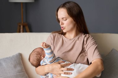 Kafkasyalı kadın, günlük kıyafetler giyip yeni doğmuş bebeğini sallıyor. Oturma odasında kanepede otururken kucağında küçük bir oğlan ya da kız çocuğu yatağa yatırıp 