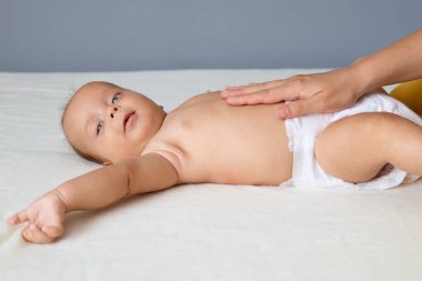 Annesi karın ağrısını önlemek için masaj yaparken, annesi de küçük, beyaz bebeğine sırt üstü masaj yapıyor.