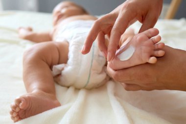 Kimliği belirsiz anne ya da bakıcı banyodan sonra bebeğe krem sürerken isimsiz bir erkek ya da kız bebek yatakta yatıyor.