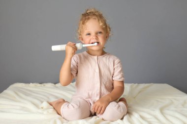 Beyaz, tatlı bir kız çocuğu diş macunu ve diş fırçasıyla yatak odasında yatarken dişlerini temizliyor.