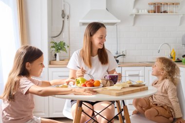 Kızlarıyla birlikte gülümseyen beyaz anne ya da akşam yemeği yemek mutfak masasında oturup anne ve çocukların sıcak ev ortamında ev yemeğinin keyfini çıkarmak.