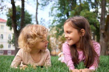 Yeşil çimenler ve ağaçlarla çevrili parkta eğlenen neşeli çocuklar baharda sıcacık havanın ve güzel manzaranın tadını çıkarıyorlar.