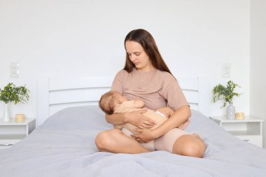 Genç bir anne, bebeğiyle veya kızıyla vakit geçirir. Çocuğa sarılır ve kucaklar. Yatakta oturur ve bebeğini emzirir.