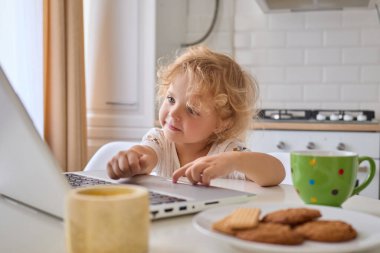 Sarışın, dalgalı saçlı, gülümseyen küçük kız evde bilgisayar ekranında çizgi film seyrediyor. Mutfaktaki masada oturmuş dijital zaman ve lezzetli atıştırmalıkların tadını çıkarıyor.