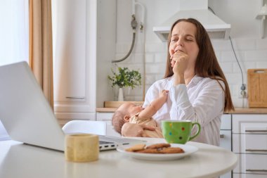 Uykucu kadın bilgisayar işinde çalışıyor ve bebeklerin online aktiviteleriyle ilgileniyor. Uzun saatler boyunca mutfak içlerinde oturup ağız kaplayarak esniyor.