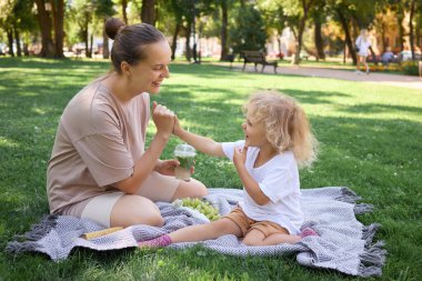 Neşeli anne ve çocuğu ağaçlarla çevrili çayırlarda oturup eğleniyorlar. Meyve ve içeceklerle pikniğin tadını çıkarıyorlar. Baharın neşesini kucaklıyorlar.