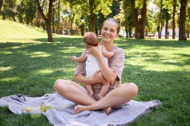Beyaz, gülümseyen genç bir kadın parkta güneşli bir pikniğin tadını çıkarıyor. Yeni doğmuş bir kız ya da oğul çimlerin üzerinde sarılıyor ve sevimli çocuk ailesi yaz bahçesinin güzellikleriyle dolu dinleniyor.