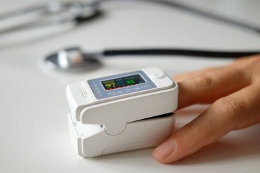 Tanınamayan bir kadın, rutin sağlık kontrolleri sırasında düzgün bir sağlık hizmeti sağlayan nabız ve doygunluğunu ölçmek için dijital parmak ucu oksimetresi kullanarak kan oksijeni seviyesini izliyor.