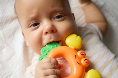 Yeni doğmuş bebek çizgili giysiler giyiyor. Tuhaf bir şekilde bakıyor ve elinde renkli bir oyuncak ısırıyor. Uyanık saatlerinde battaniyeye uzanıp oynuyor.