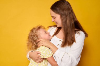 Neşeli kadın ve bebek sarı arka planda duruyor. Anne kızına sarılıyor. Sevgi ve mutluluk gösteriyor.