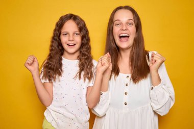 Son derece mutlu bir kız ve annesi sevinçle gülüyor ve tezahürat yapıyorlar. Kapalı alanda coşkulu jestler yapıyorlar. Sarı arka planda zaferlerini kutluyorlar.