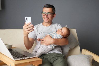 Babam, akıllı telefondan video görüşmesinde yenidoğan ile selfie çekiyor. Evde çalışıyor, ebeveynlik yapıyor ve bilgisayardaki iş görevlerini dengeliyor. Evdeki kanepede uzaktan kumandayla idare ediyor.