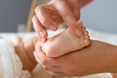 Tanımlanamayan anne, yeni doğan bebeğinin sağlıklı gelişmesi için bebeğinin ayaklarına masaj yapıyor.