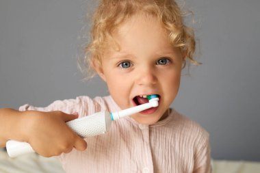 Diş fırçasını diş macunuyla tutan sevimli bayan bebek çocukluğunda sağlıklı diş hijyenini geliştirmek için dişlerini fırçalama alışkanlığının tadını çıkarıyor.