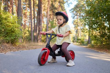 Parktaki patika boyunca ilk bisikletini süren sevimli çocuk yaz tatilinin tadını çıkarırken aynı zamanda eğlenceli açık hava aktiviteleri sırasında dengeyi ve koordinasyonu geliştiriyor.